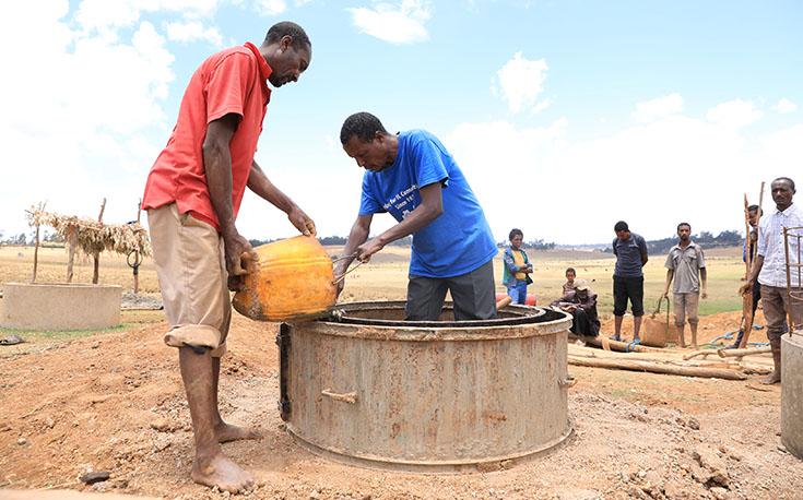 Zwei Männer gießen die Betonringe für den Brunnen, dabei ist besondere Sorgfalt gefragt. (Foto)